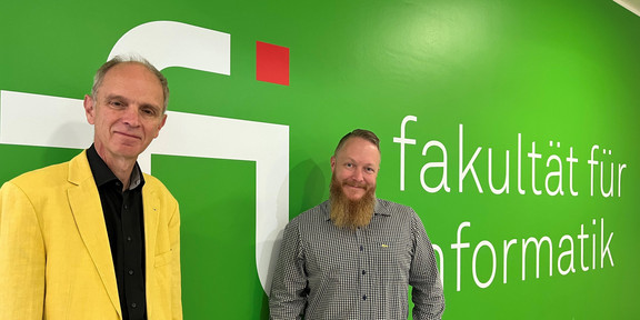 Auf dem Bild stehen Prof. Dr. Gernot Fink und Herr Dr. Lukas Rehm vor einer grünen Wand