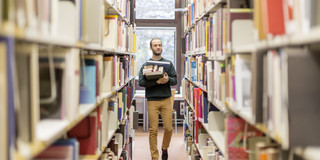 Schmuckbild - Mann läuft in Bibliothek mit Büchern auf dem Arm