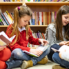 Vier Grundschülerinnen und Grundschüler sitzen vor einem Bücherregal am Boden und lesen gemeinsam in Büchern