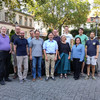 12 Personen stehen für die Fotoaufnahme auf einem Parkplatz. Im Hintergrund sind alte Gebäude zu sehen.