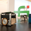 In the foreground small cube-shaped robots, in the background the logo of the Faculty of Computer Science