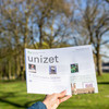 A hand is holding the current issue of the campus newspaper unizet up in the air.