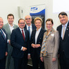 A group of men and women in suits smile at the camera in front of a UA Ruhr poster.