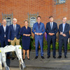 A woman and seven men stand side by side for a group photo outside a building.