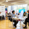 In a large room there are many tables where people are having conversations