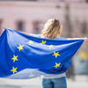 A woman is holding a European flag with her hands outstretched, waving it behind her back.