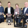 Four people stand next to each other at a table on which a 3D printer is placed.