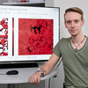 Photo of Raphael Fischer. He is sitting in front of a screen showing two satellite images.