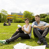 Eine Studentin und ein Student sitzen auf einer Wiese auf dem Campus.